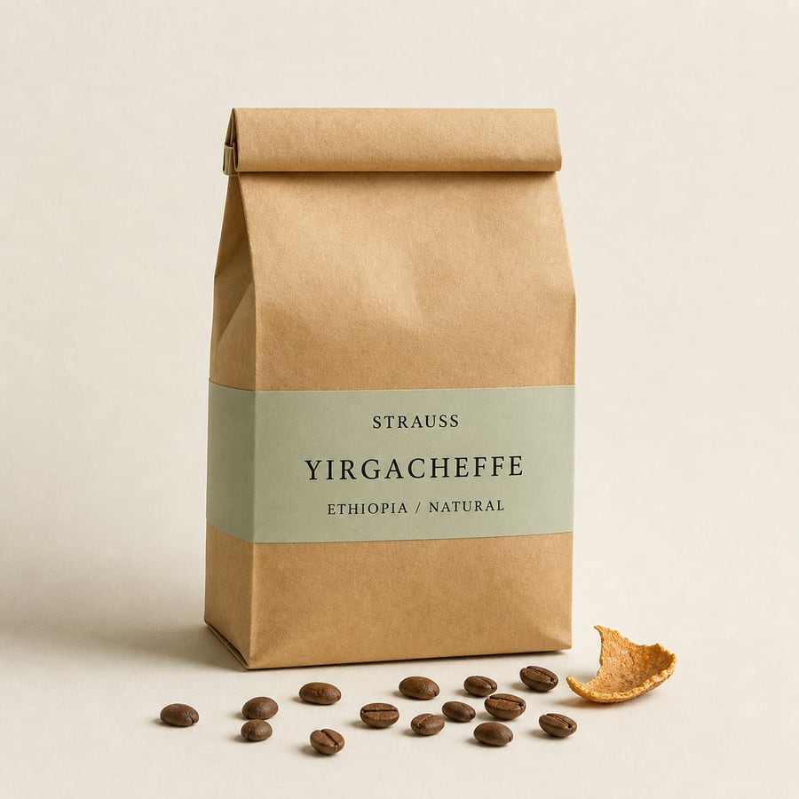 Strauss Yirgacheffe bag with a pale sage label band, small props of coffee beans and dried citrus peel on warm paper.